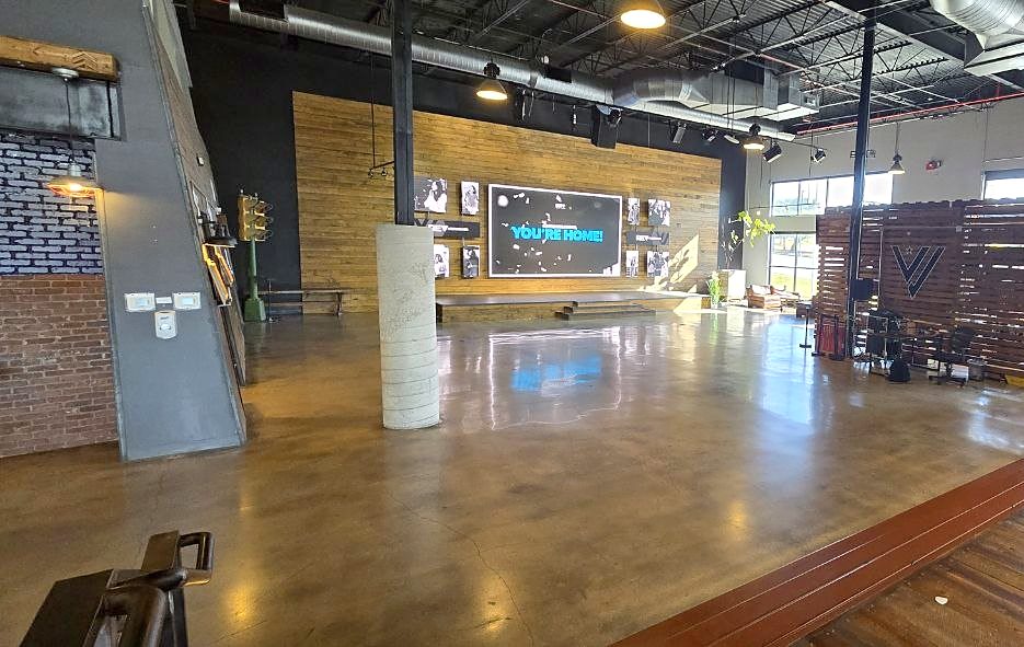 The open REV Mortgage office floor, with a raised stage in front of a reclaimed-wood wall and a lit screen reading You're Home